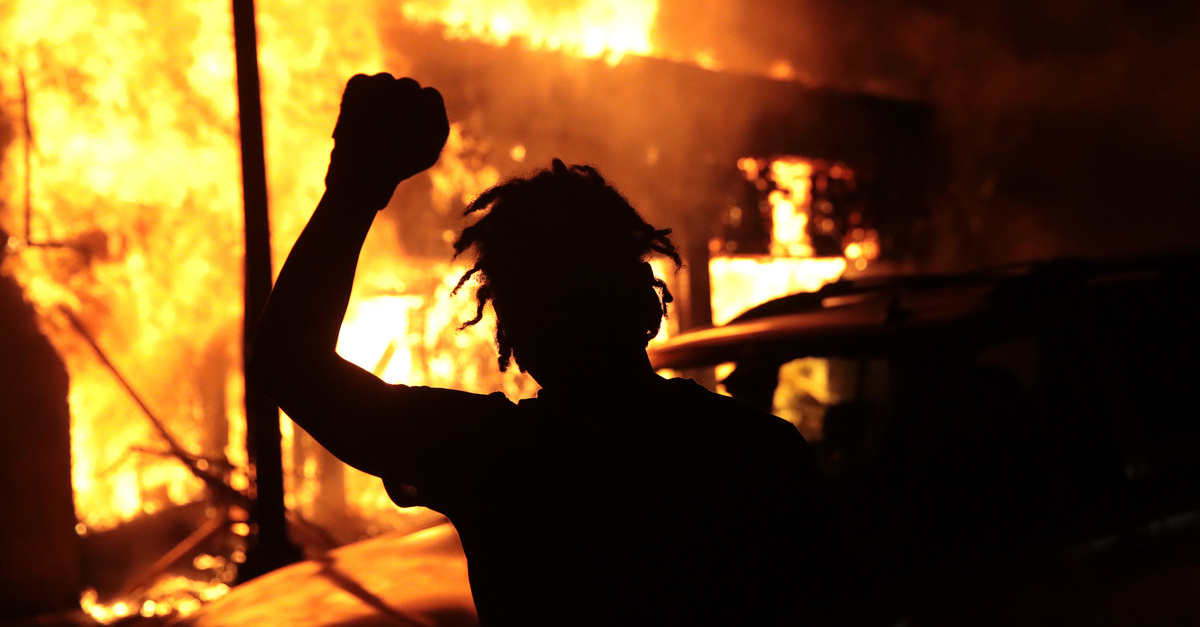 MINNEAPOLIS, MINNESOTA - MAY 29: A man raises his fist in front of a burning building during protests sparked by the death of George Floyd while in police custody on May 29, 2020 in Minneapolis, Minnesota. Earlier today, former Minneapolis police officer Derek Chauvin was taken into custody for Floyd's death. Chauvin has been accused of kneeling on Floyd's neck as he pleaded with him about not being able to breathe. Floyd was pronounced dead a short while later. Chauvin and 3 other officers, who were involved in the arrest, were fired from the police department after a video of the arrest was circulated. 