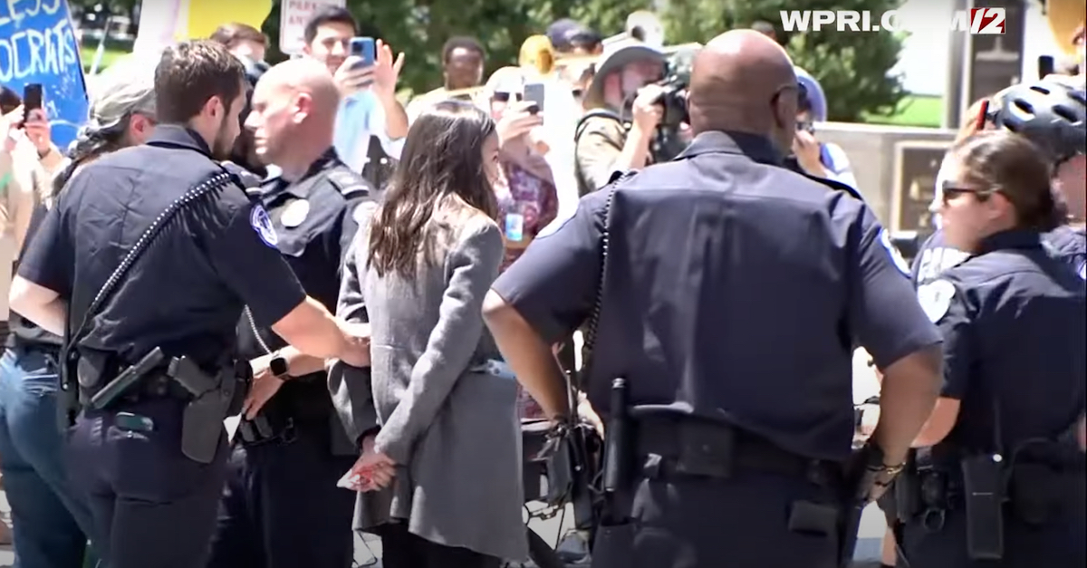 Rep. Alexandria Ocasio-Cortez (D-N.Y. 14) was not handcuffed as Capitol Police officers led her away from a street protest near the U.S. Supreme Court. (Image via WPRI-TV/YouTube screengrab.)