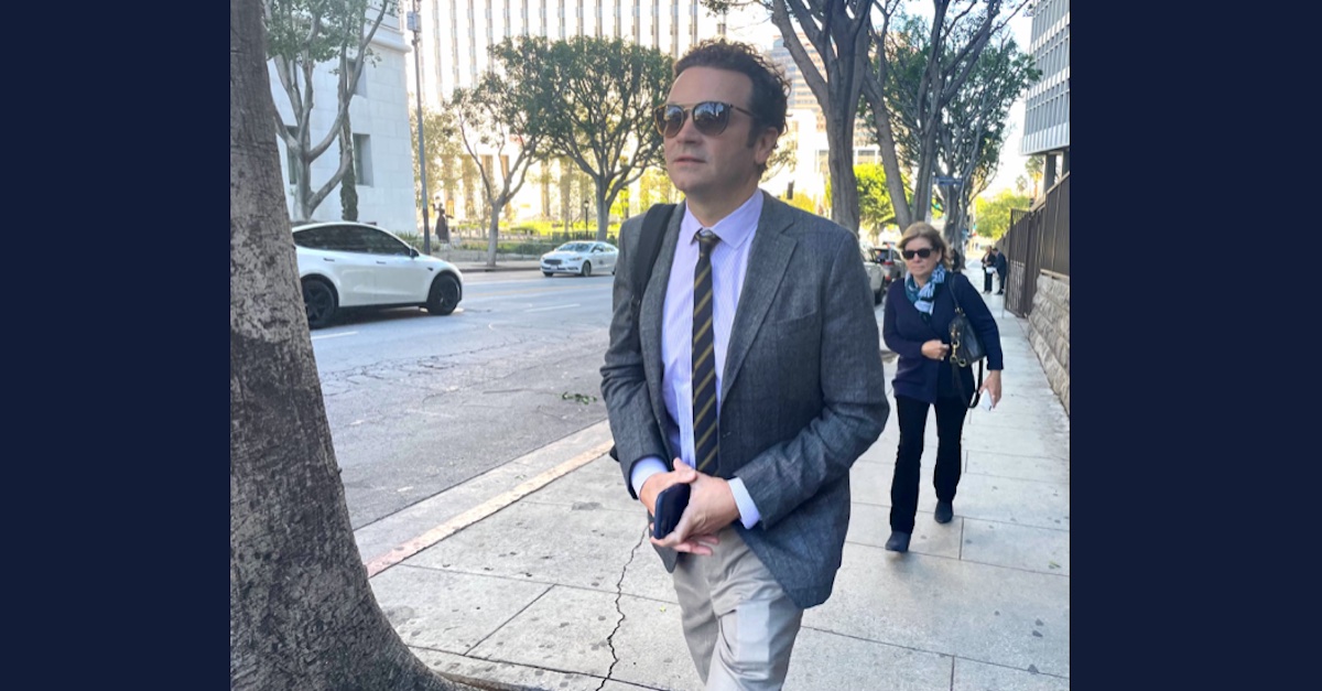 Actor Danny Masterson walks on a sidewalk wearing sunglasses, pants, a white collared shirt, a sport coat and a tie