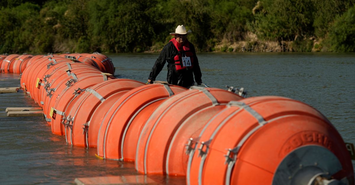 A kayaker walks past large buoys being used as a floating border barrier on the Rio Grande, Aug. 1, 2023, in Eagle Pass, Texas (AP Photo/Eric Gay).